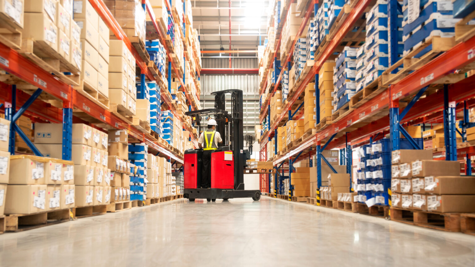 worker in forklift truck loading packed goods in huge distributi
